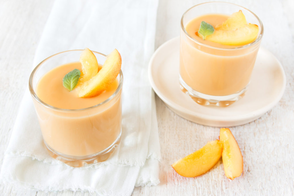 Peach dessert in portion glasses with peach slices and mint on white wooden table, close up, horizontal