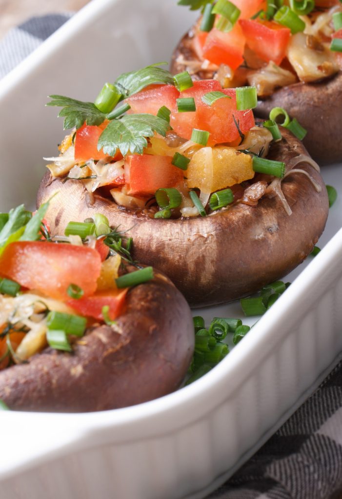 Vegetarian cuisine: stuffed portobello mushrooms with vegetables closeup at the table.