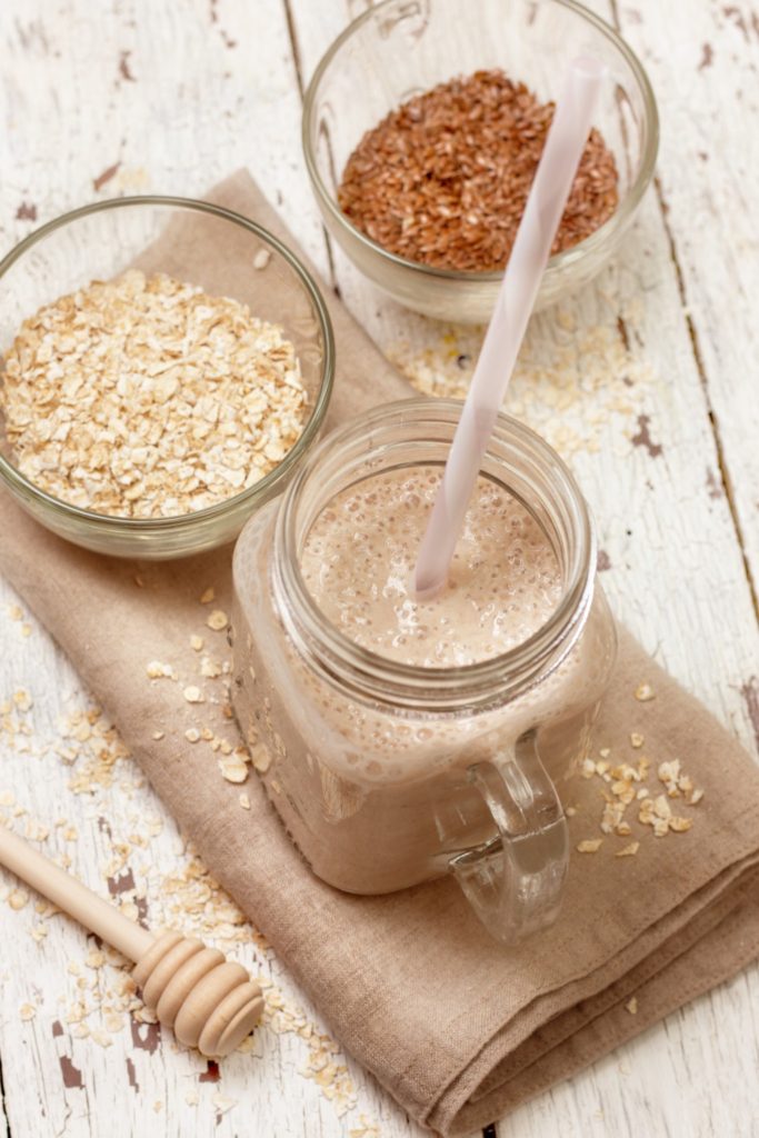 Smoothies with milk (soy, almond, coconut), oatmeal and flax seeds on a wooden background (top view)