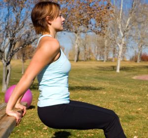 Young woman performing tricep dips on a bench.