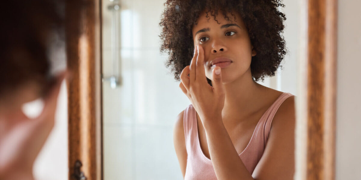 Woman with curly hair applying makeup in front of a bathroom mirror.