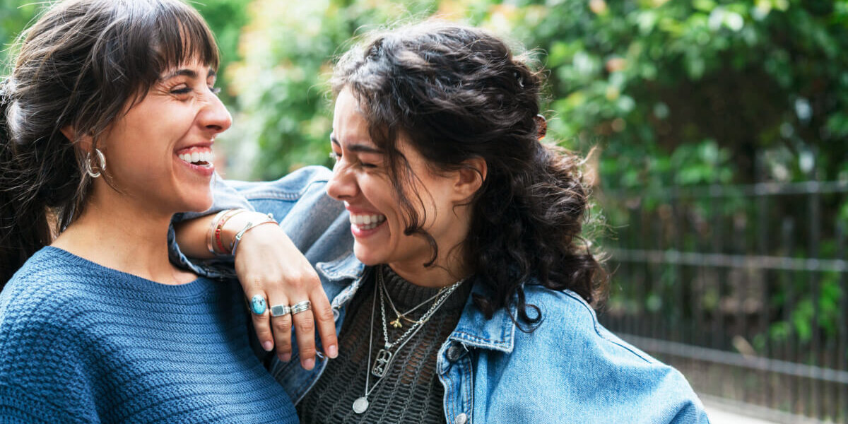 Two women smiling and embracing outdoors.