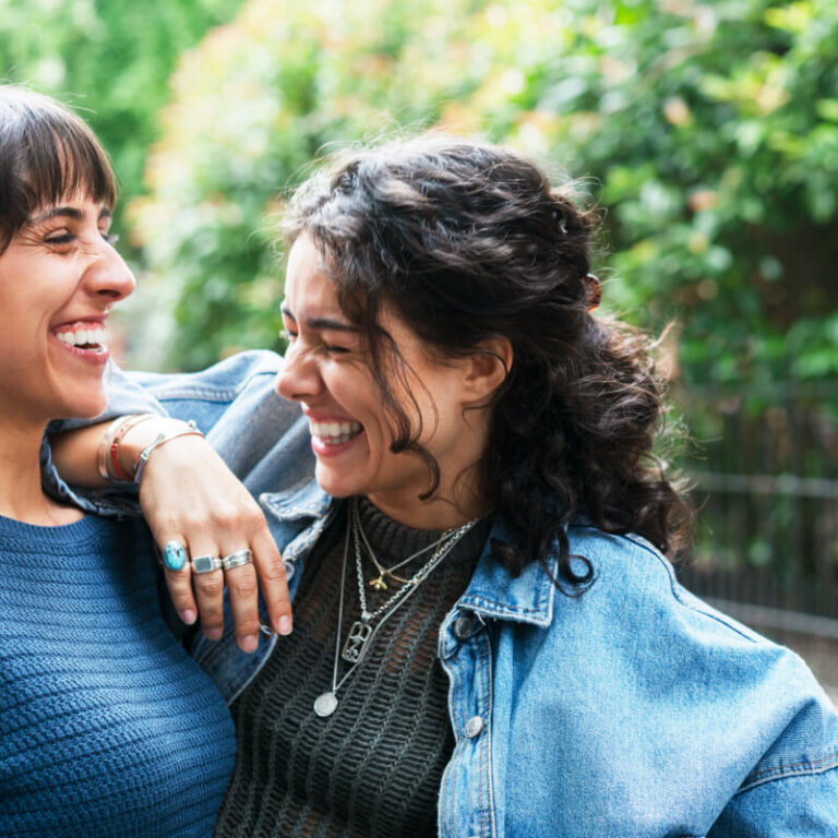 Two women smiling and embracing outdoors.