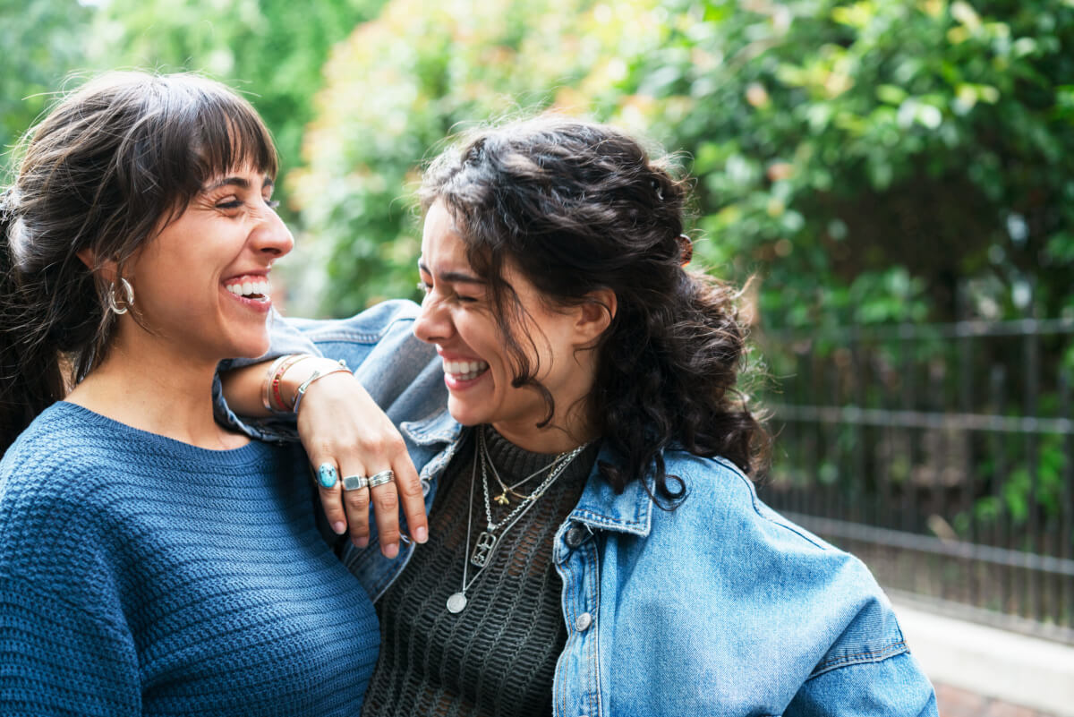Two women smiling and embracing outdoors.