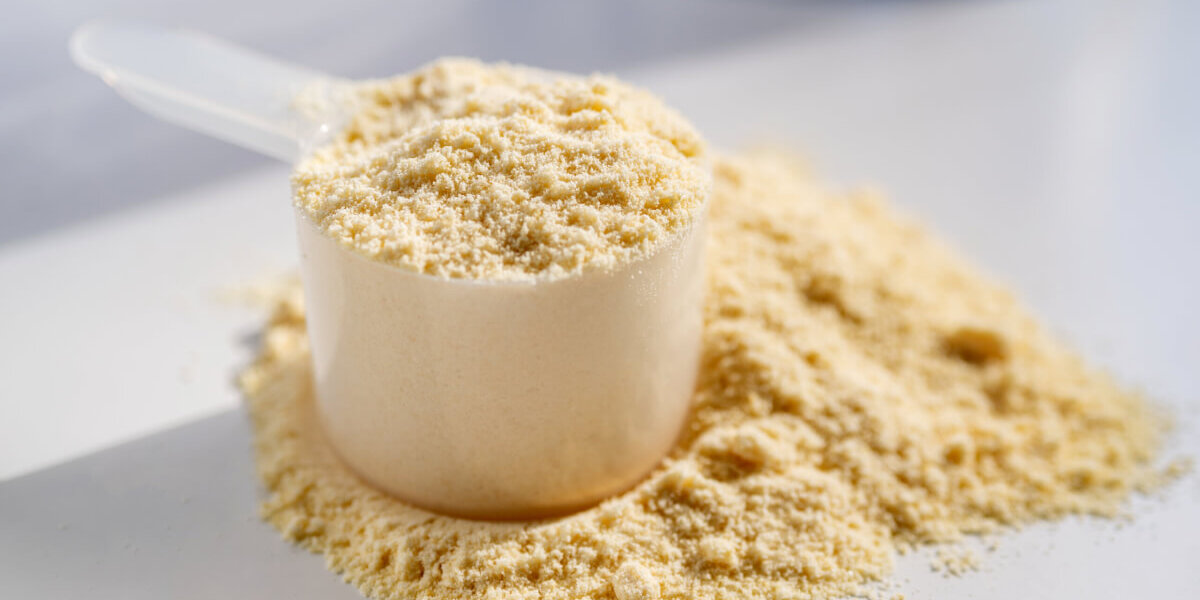 A white measuring cup filled with pale yellow powder, with powder scattered around on a light surface.