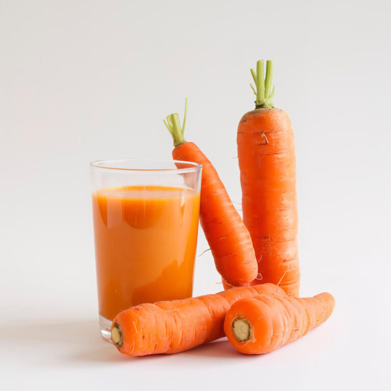 A glass of carrot juice sits beside several fresh carrots on a white background.