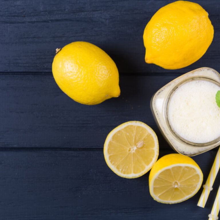 Lemons and a jar of lemonade with striped yellow straws and a mint garnish on a dark wooden surface.