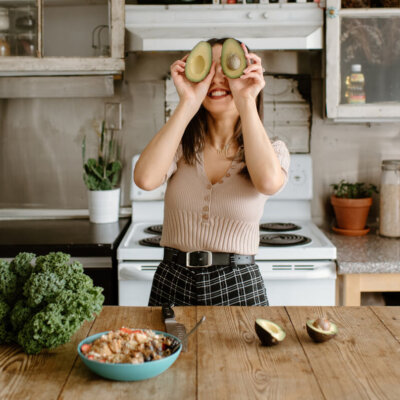 Smiling young woman holding avocado in front of face