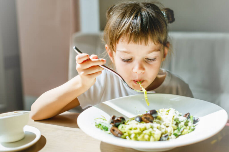 Young child happily eating a bowl of pesto pasta, with green sauce visible on the noodles, illustrating a creative way to incorporate more vegetables into meals. "Young child happily eating a bowl of pesto pasta, with green sauce visible on the noodles, illustrating a creative way to incorporate more vegetables into meals."