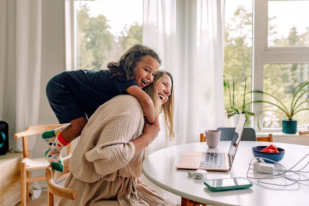 Happy mature mother carrying son on shoulders while sitting on chair near table at home
