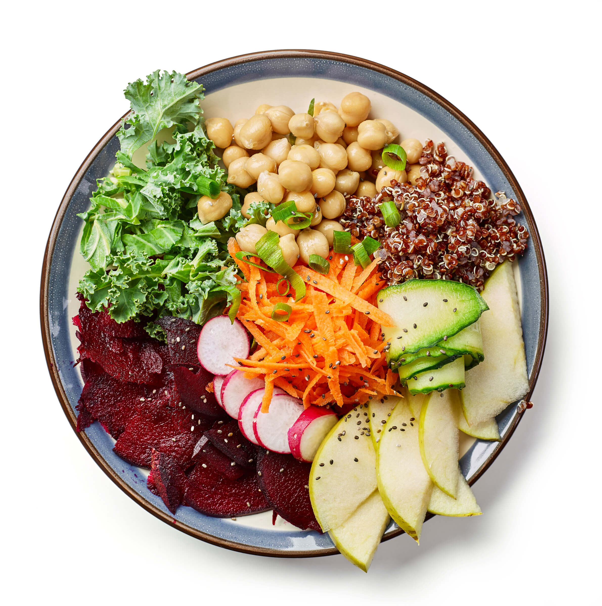 A round plate of colorful vegetarian salad with kale, chickpeas, red quinoa, beets, shredded carrots, radishes, cucumber, and pear slices.