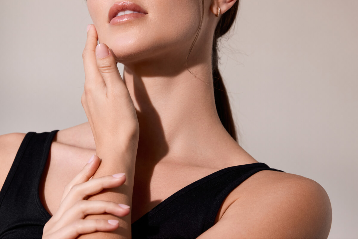 Close-up of a woman's neck and lower face with her hands resting on her neck.